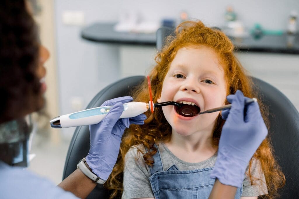 A child sitting calmly in a pediatric dentist's chair, holding a stuffed animal.