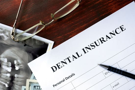 A dental insurance form next to glasses on a brown wooden table