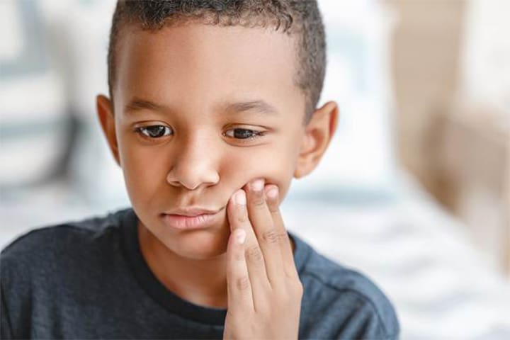 A child holding their mouth because they have a toothache