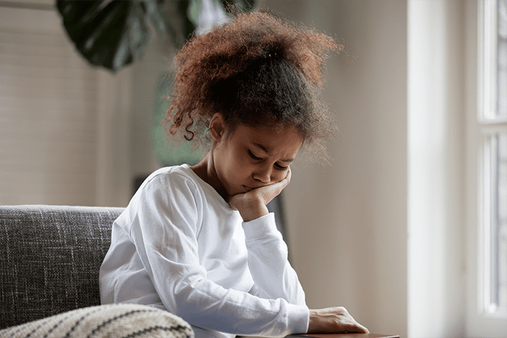 A child sitting on a couch and holding her face because she has a toothache