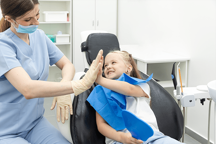 A dentist giving a high-five to a child while they’re sitting in a dental chair