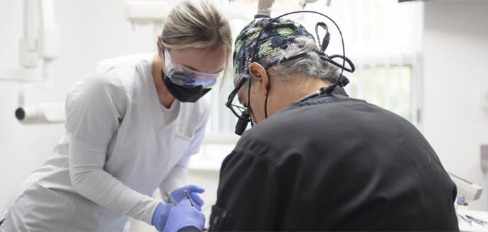 Dentists in protective gear focus on a procedure in a bright, clinical setting.
