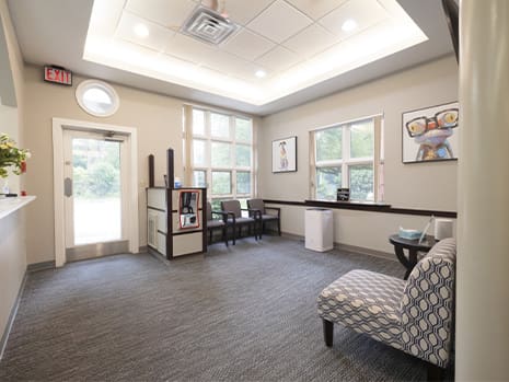 A waiting room at Waban Dental Group featuring a couch and several chairs for patients.