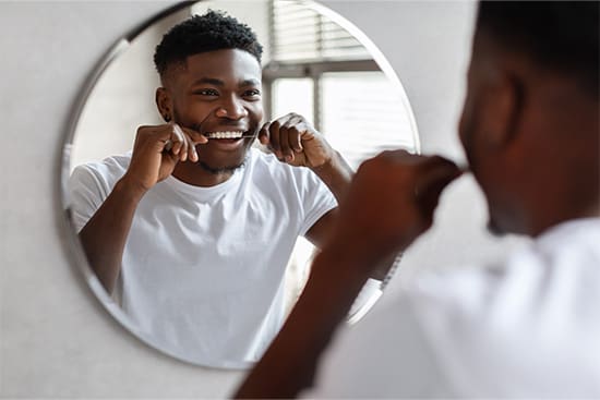 Patient smiling while flossing his teeth in bathroom.