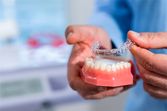 Dentist putting clear aligner on model of teeth.