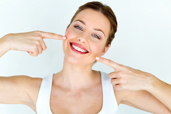 Woman in white tank top pointing at whiter smile.