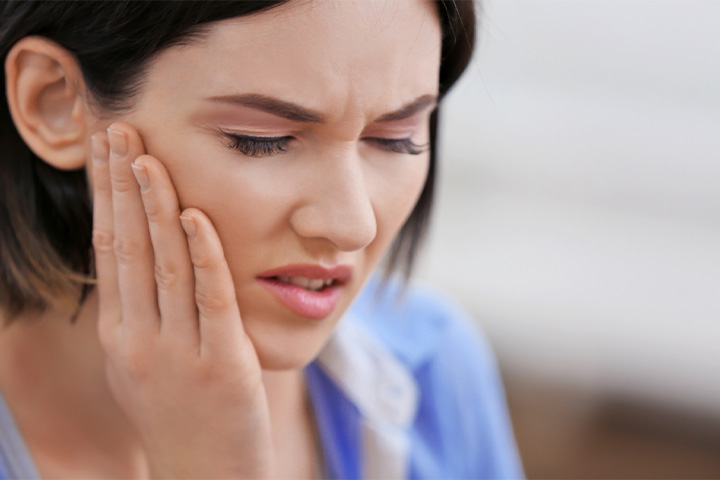 Close-up of woman rubbing her jaw in pain.