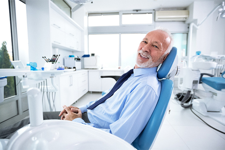 Older man with tie leaning back in dental chair.