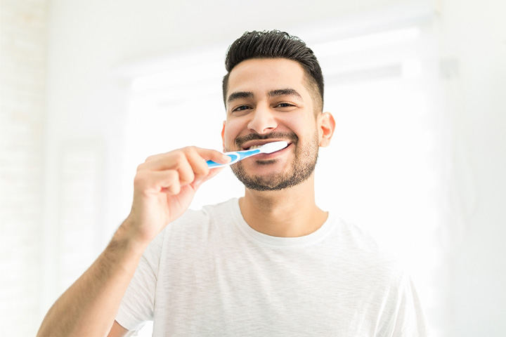 Man smiling while brushing his teeth.