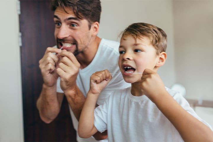 Father and son flossing together over sink.
